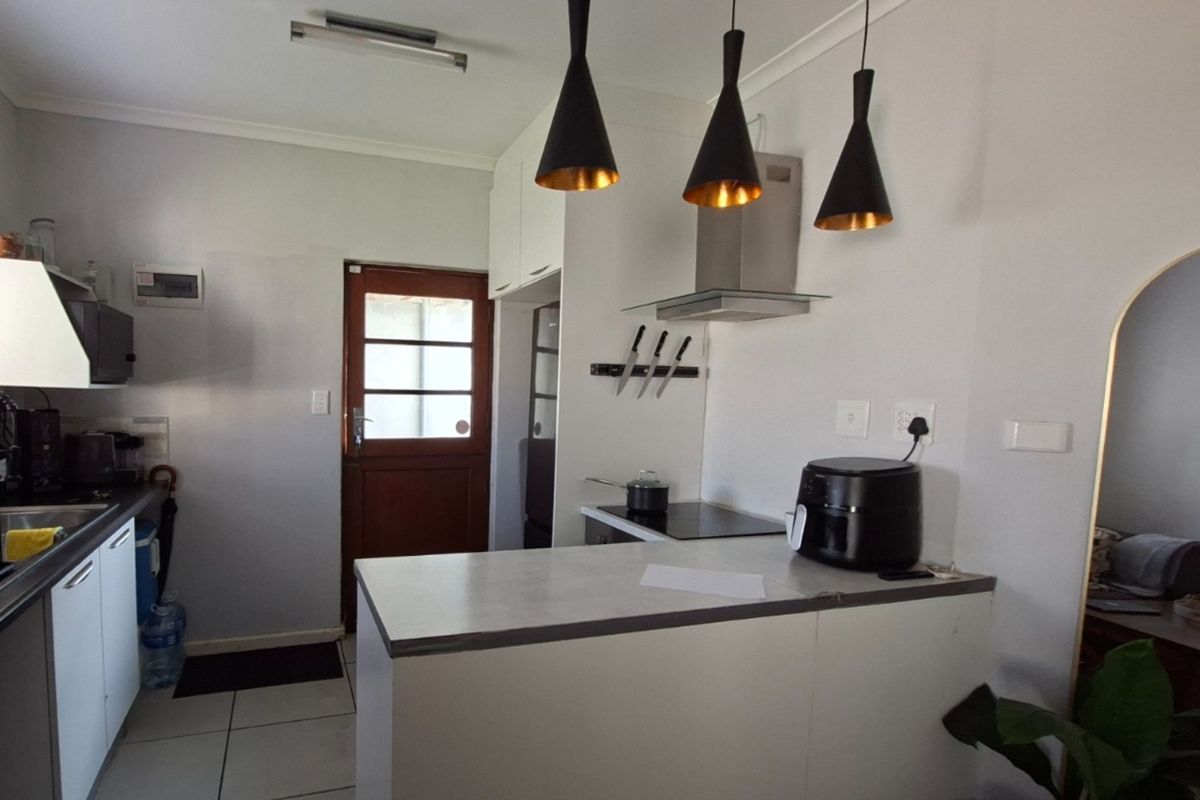 A functional kitchen featuring white cabinetry, laminate countertops, a built-in electric hob with extractor fan, and tiled flooring with direct exterior access.