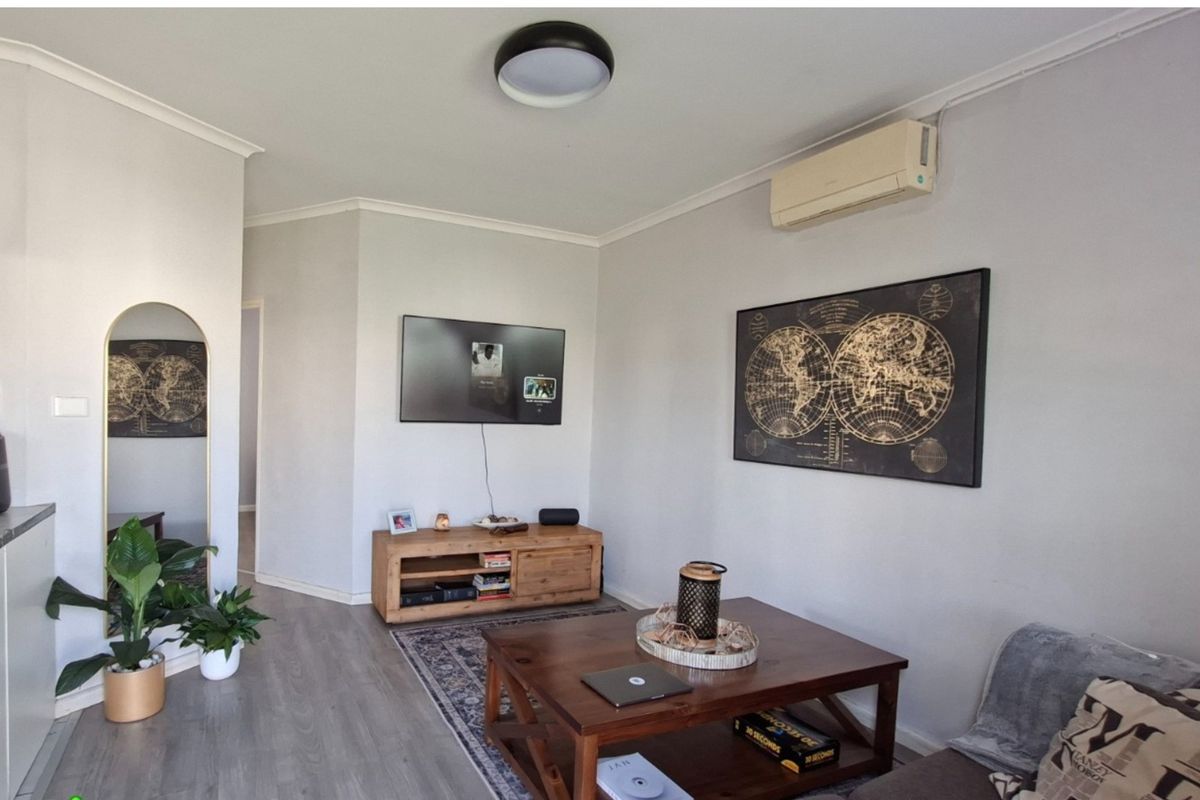 A well-maintained living room featuring modern laminate flooring, a wall-mounted air conditioning unit, and neutral wall finishes.