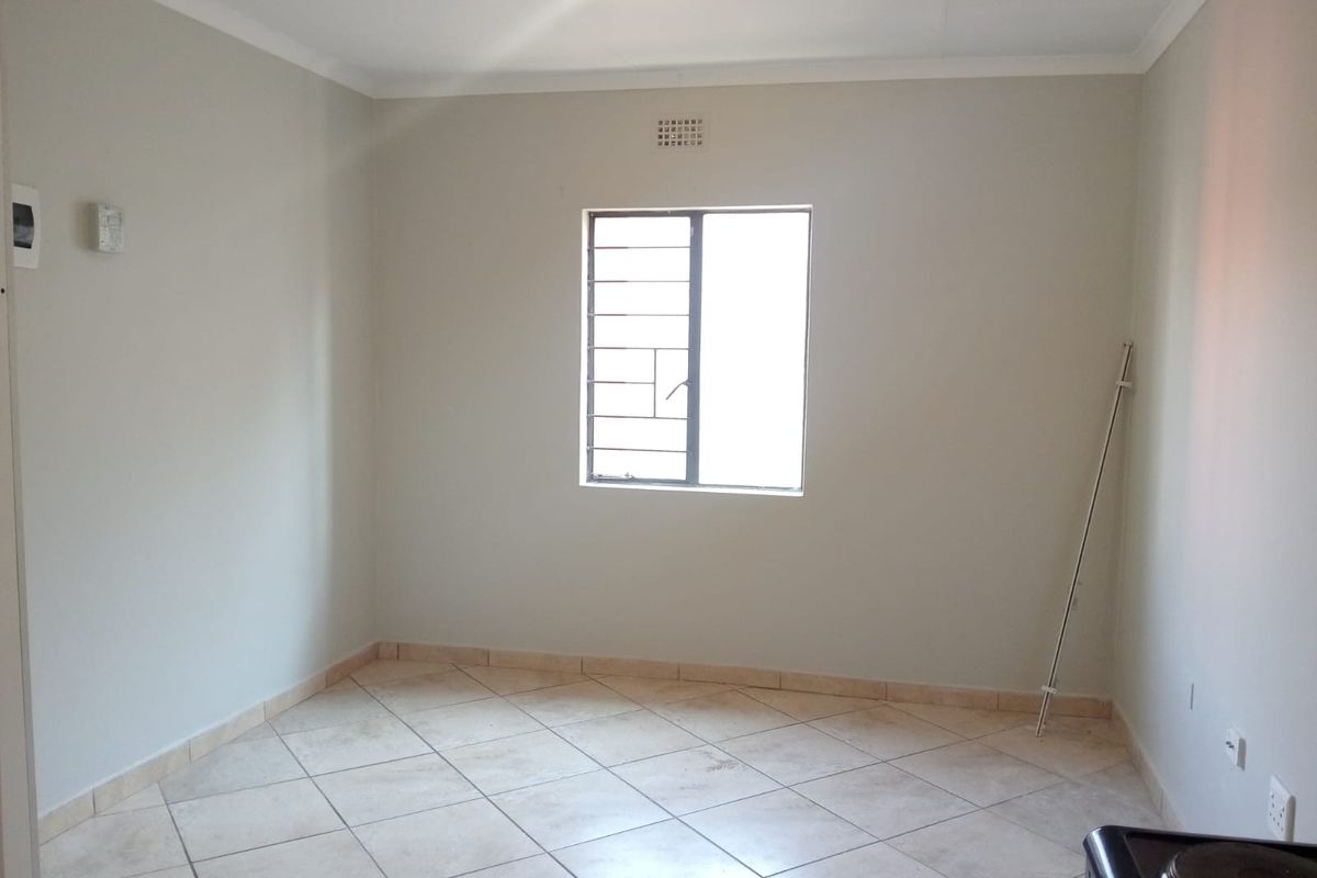 An empty bedroom featuring neutral wall paint, tiled flooring, and security bars on the window, providing a blank canvas for personalization.