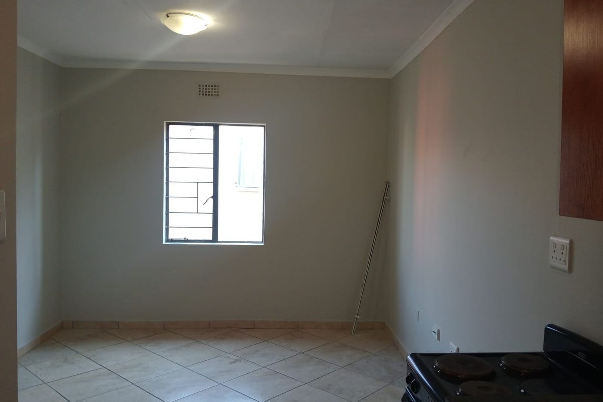 An empty kitchen area featuring tiled flooring, a window with security bars, and a built-in stove.