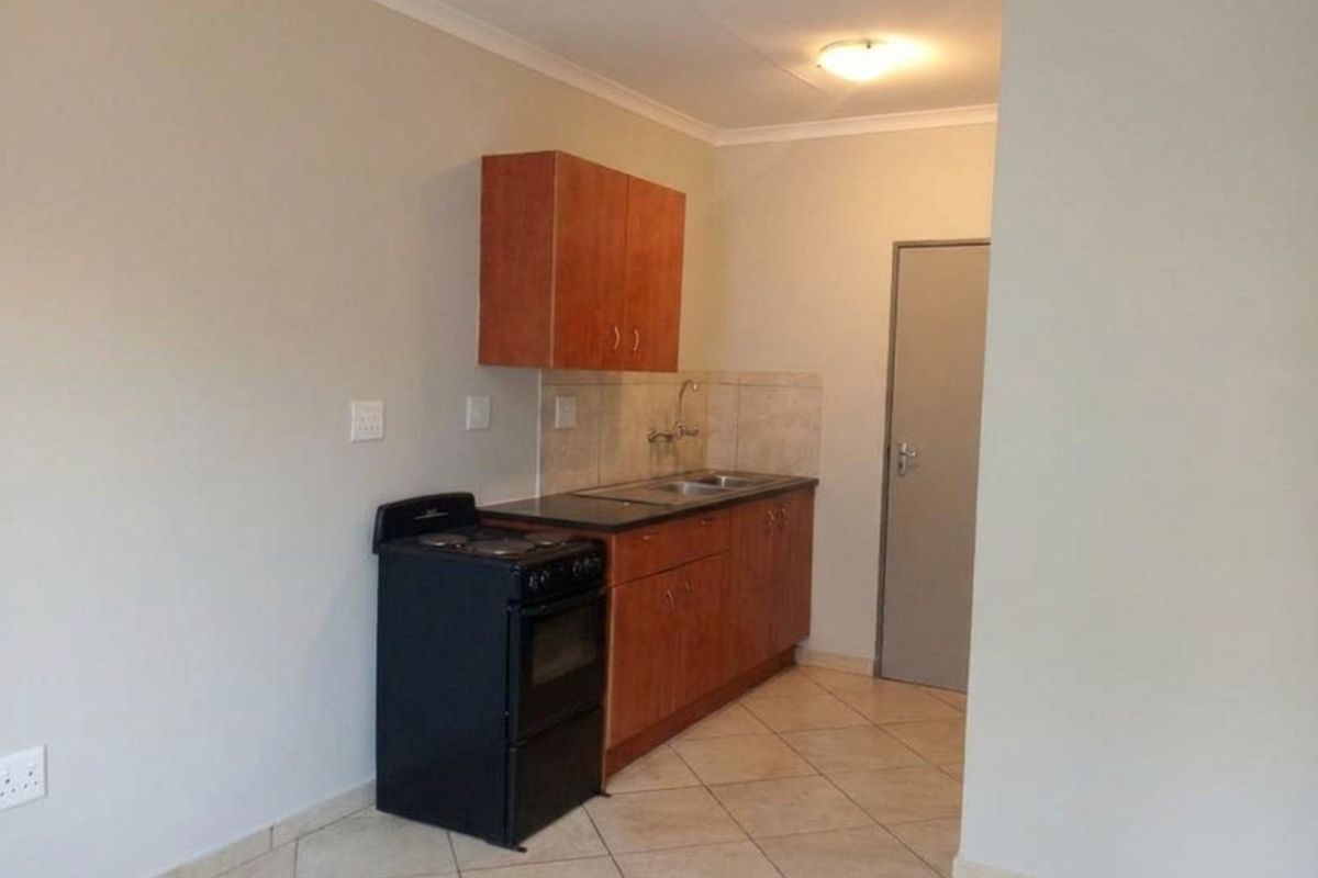 A compact kitchen featuring wooden cabinetry, laminate countertops, a stainless steel sink, tiled backsplash, and ceramic floor tiles.