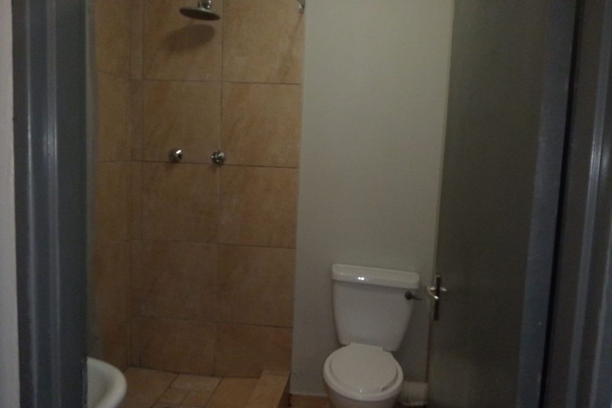 A compact bathroom featuring a tiled shower enclosure and a standard toilet, requiring cosmetic updates to improve the overall aesthetic.