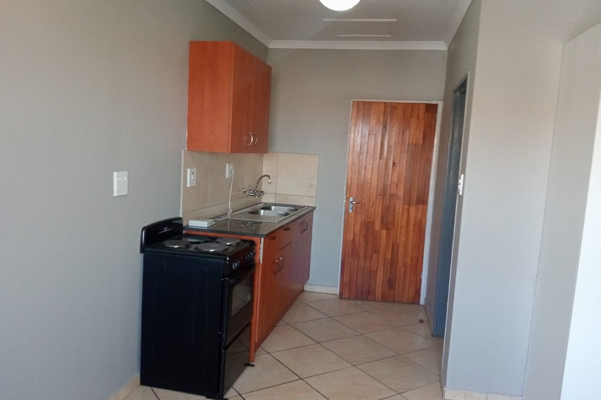 A functional kitchen area featuring built-in cabinetry, a stainless steel sink, tiled splashback, and a freestanding stove with tiled flooring throughout.