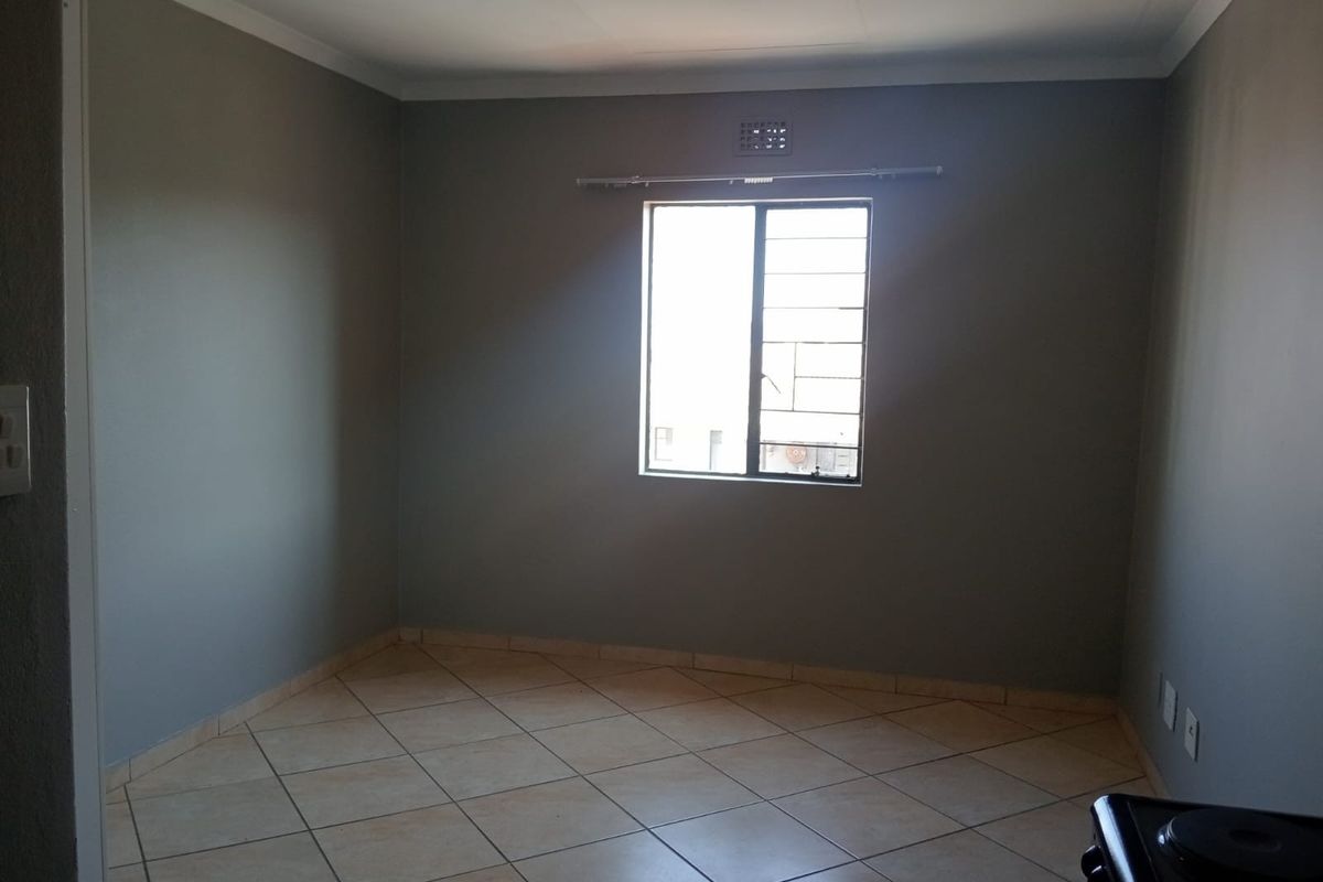 A vacant bedroom featuring neutral grey walls, tiled flooring, and a window fitted with security bars.