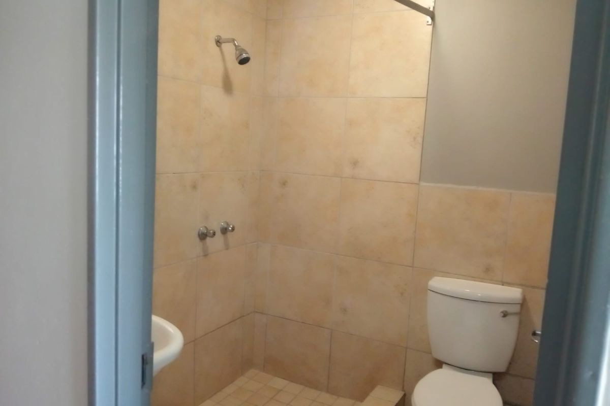 A functional bathroom featuring a shower area with tiled walls, a pedestal basin, and a standard toilet.