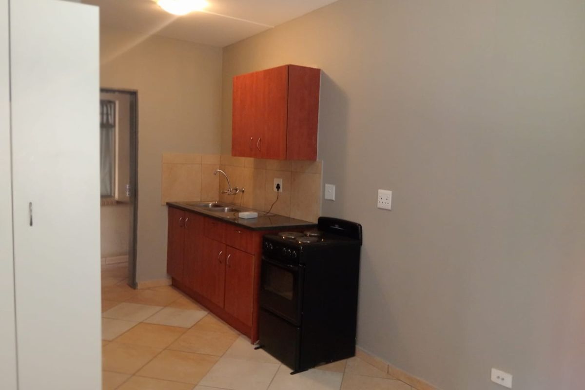 A compact kitchen area featuring wooden cabinetry, a stainless steel sink, tiled backsplash, and a freestanding stove with tiled flooring.