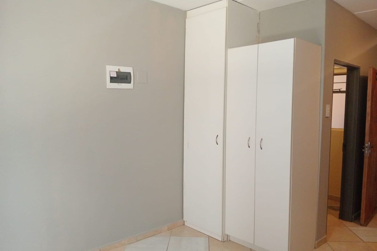 A functional bedroom space featuring built-in white cupboards, tiled flooring, and a wall-mounted electrical distribution board.