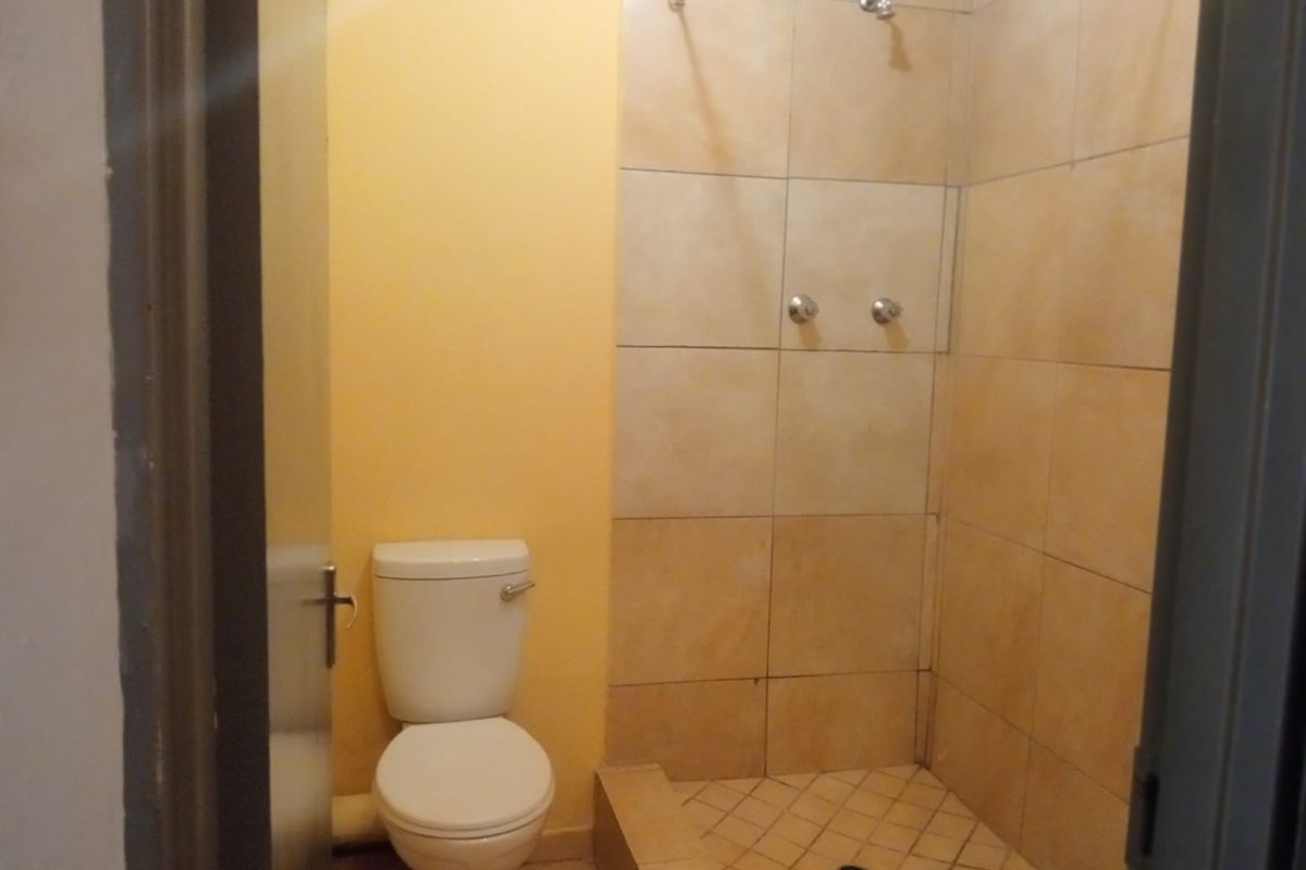 A functional bathroom featuring a toilet and a tiled shower enclosure with wall-mounted fixtures.