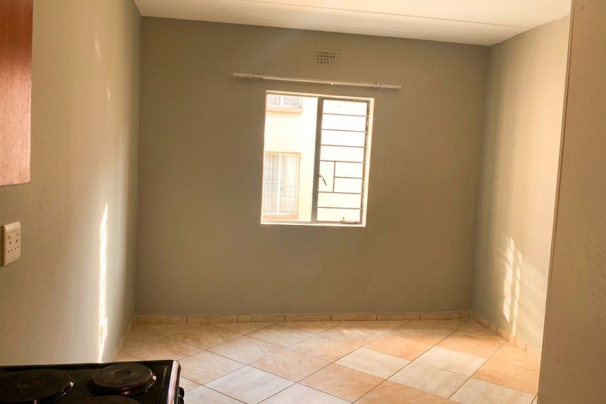 An empty kitchen area featuring tiled flooring, a window with security bars, and a built-in electric stove.