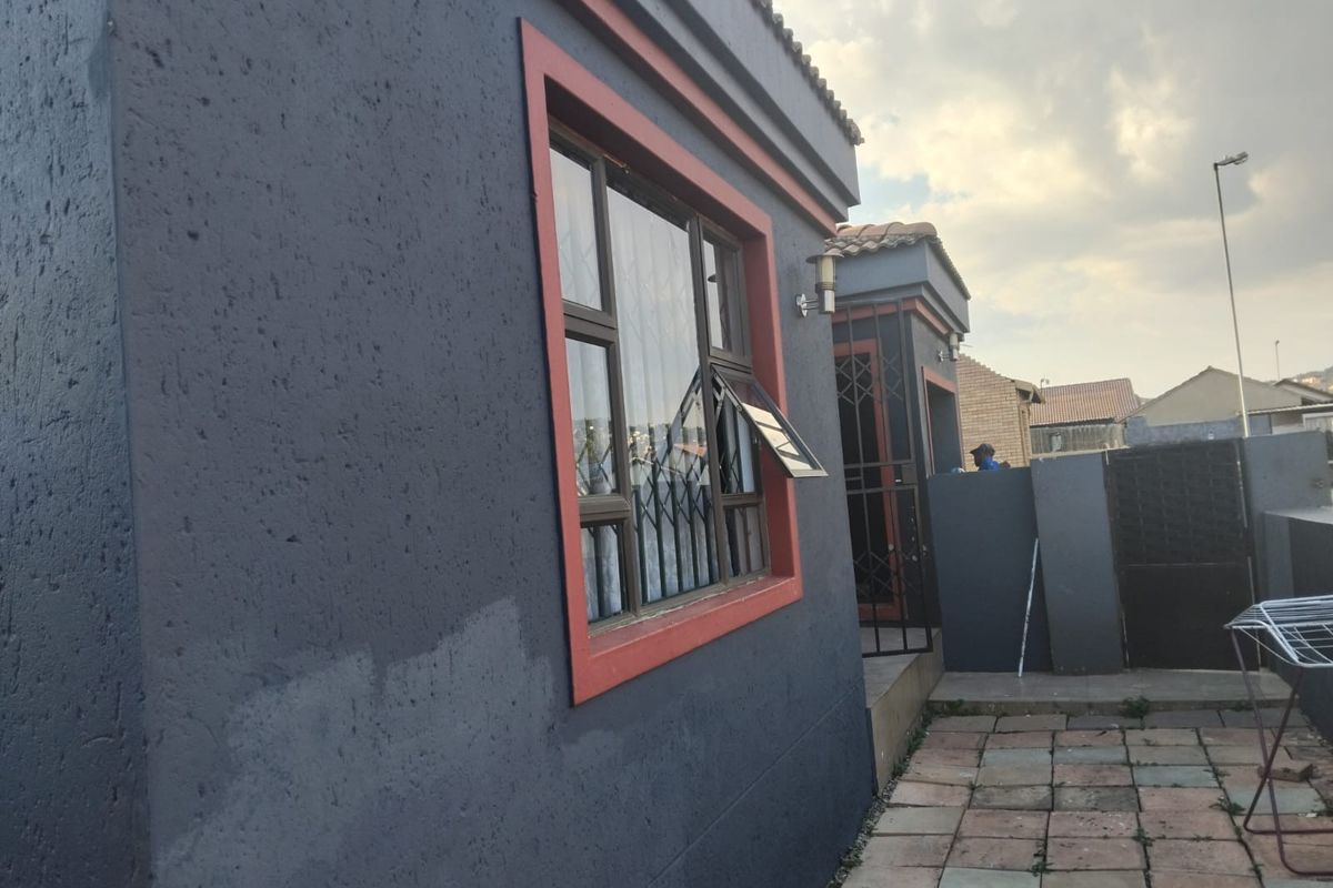 Rear exterior view of the apartment featuring a paved patio area, security gates, and security bars on the windows.