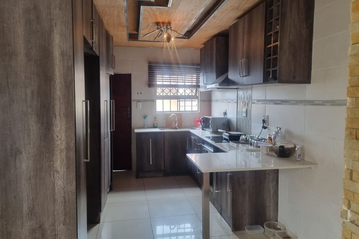 Modern kitchen featuring dark wood-grain cabinetry, stone countertops, a breakfast bar, tiled backsplash, and integrated hob with extractor fan.