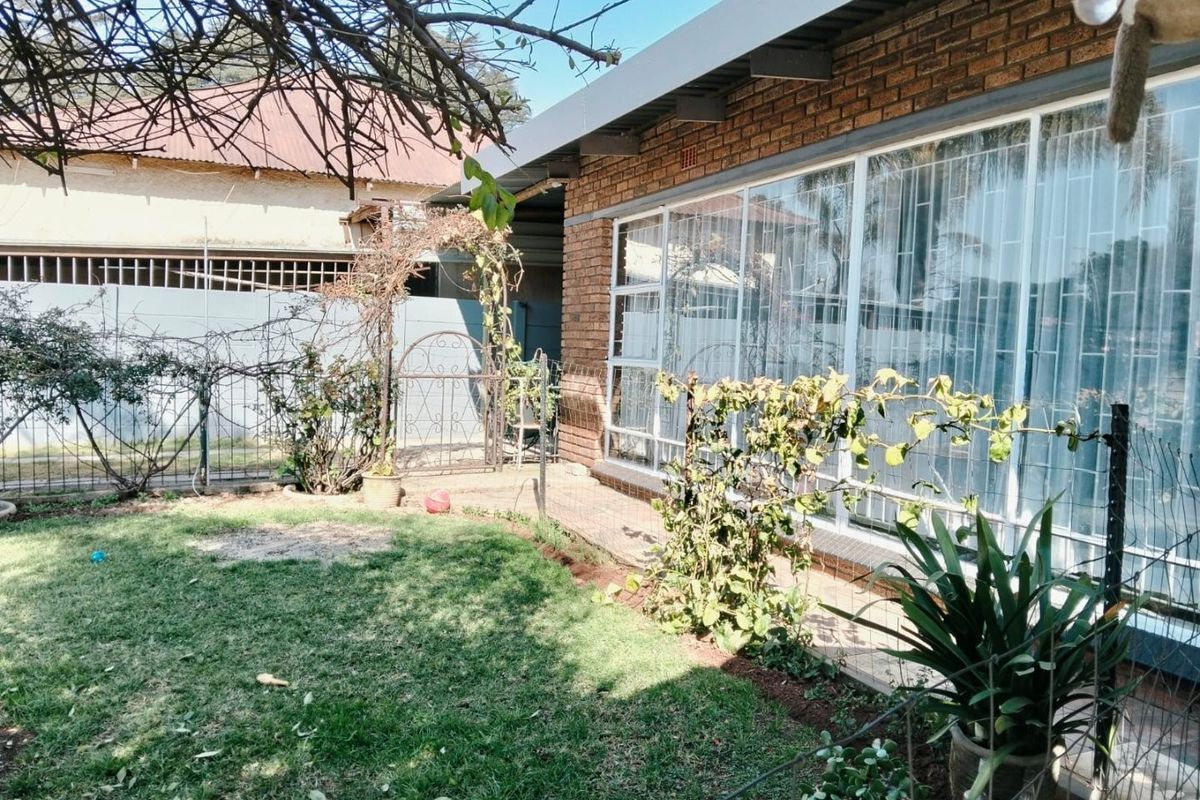 A view of the rear exterior featuring a brick facade, large windows with security bars, and a small garden area with lawn.