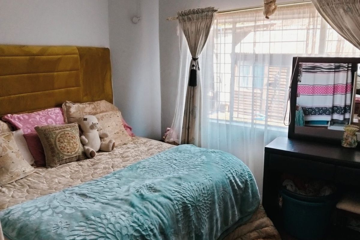 A functional bedroom featuring a window with security bars and a ceiling ventilation unit.