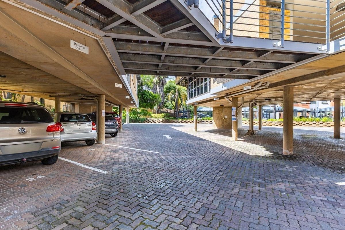 Covered commercial parking area featuring paved ground, concrete support columns, and an overhead steel staircase structure.