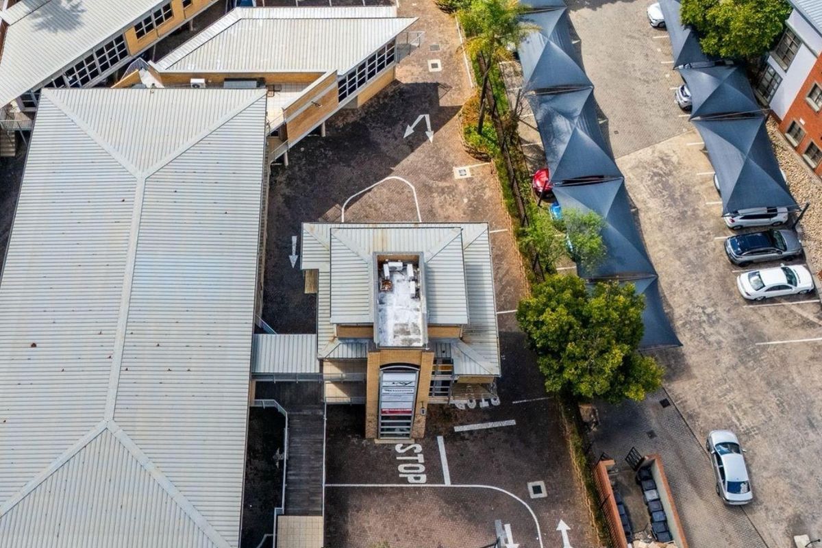 Aerial view of a commercial property complex featuring multiple buildings with metal roofing, extensive paved parking areas, and covered shade cloth carports.