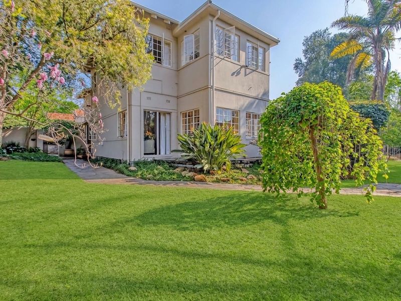 A well-maintained double-story residential property featuring a lush green garden and stone paved pathways leading to the rear entrance.