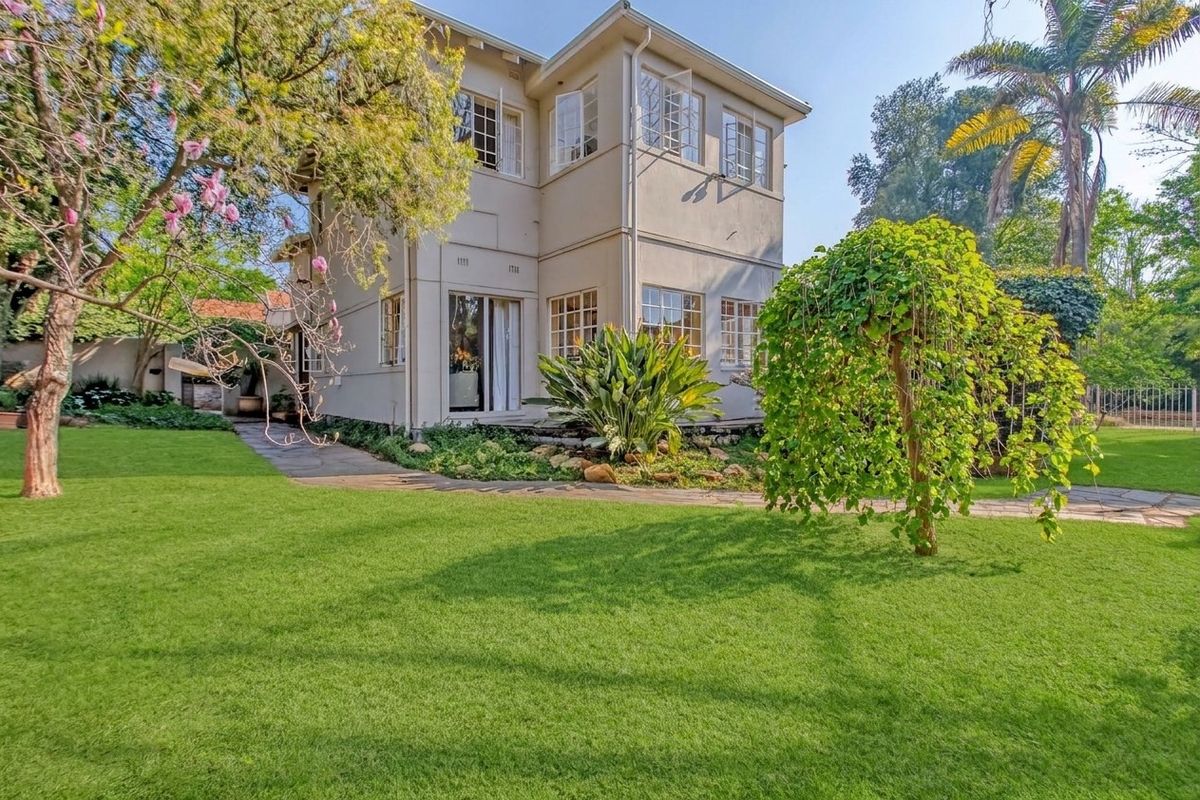 A well-maintained double-story residential property featuring a lush green garden and stone paved pathways leading to the rear entrance.