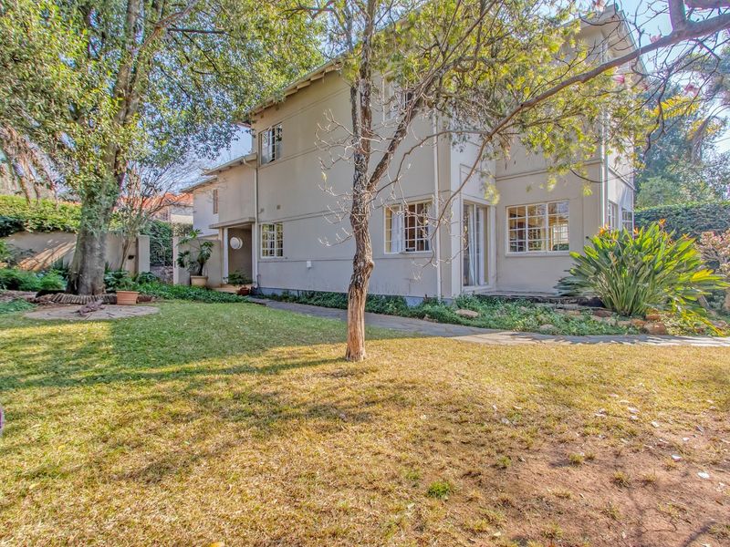 Rear view of the two-story house featuring a landscaped garden, paved walkway, and multi-pane windows.