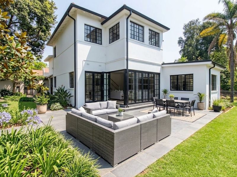 A well-maintained rear exterior view featuring a paved patio, landscaped garden, and modern black-framed folding doors providing seamless indoor-outdoor flow.