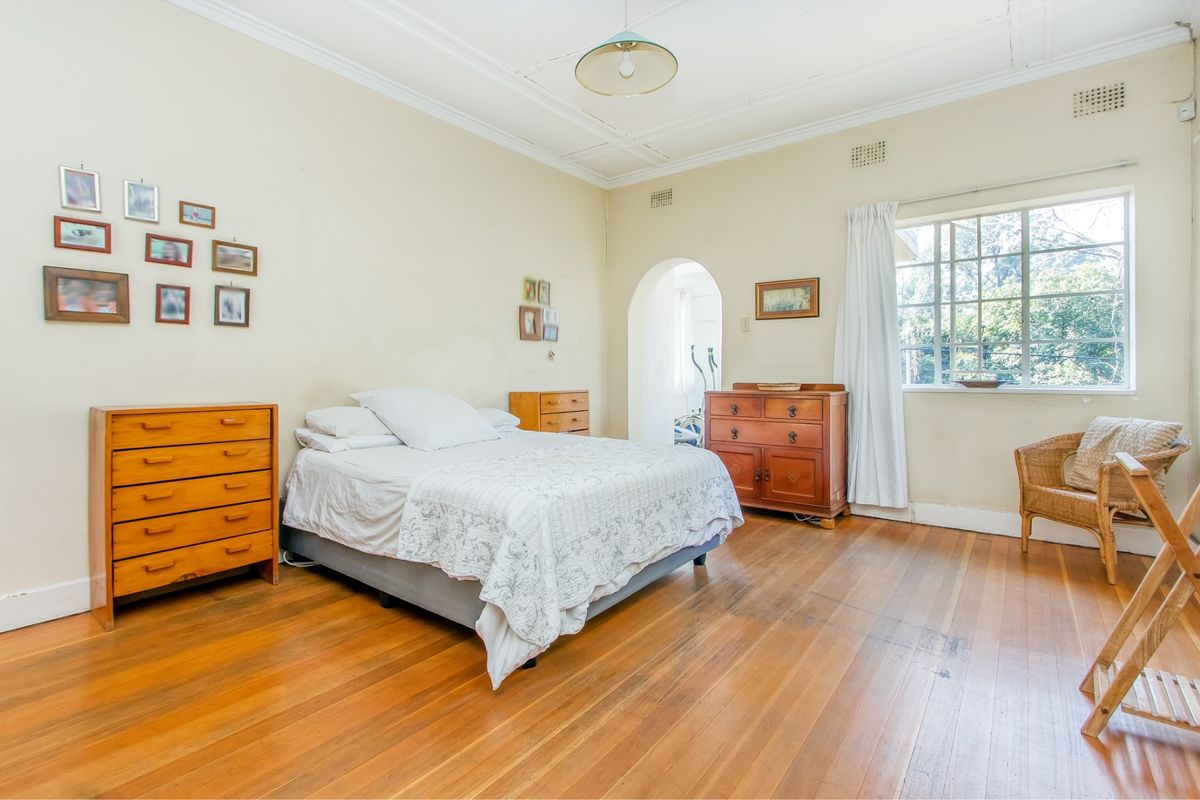 Spacious bedroom featuring original hardwood flooring, classic ceiling cornicing, and an arched doorway leading to an adjoining space.