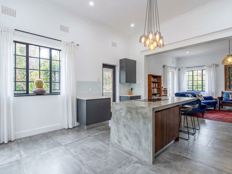 Modern open-plan kitchen featuring a concrete island, sleek cabinetry, and large format floor tiles, seamlessly flowing into the adjacent living area.
