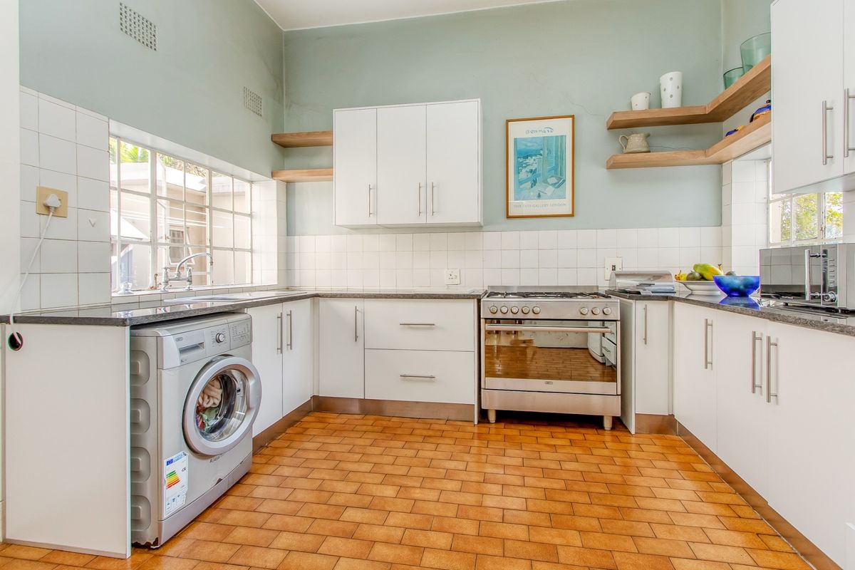 A functional kitchen featuring white cabinetry, granite countertops, a stainless steel stove, and classic terracotta floor tiles with ample natural light.