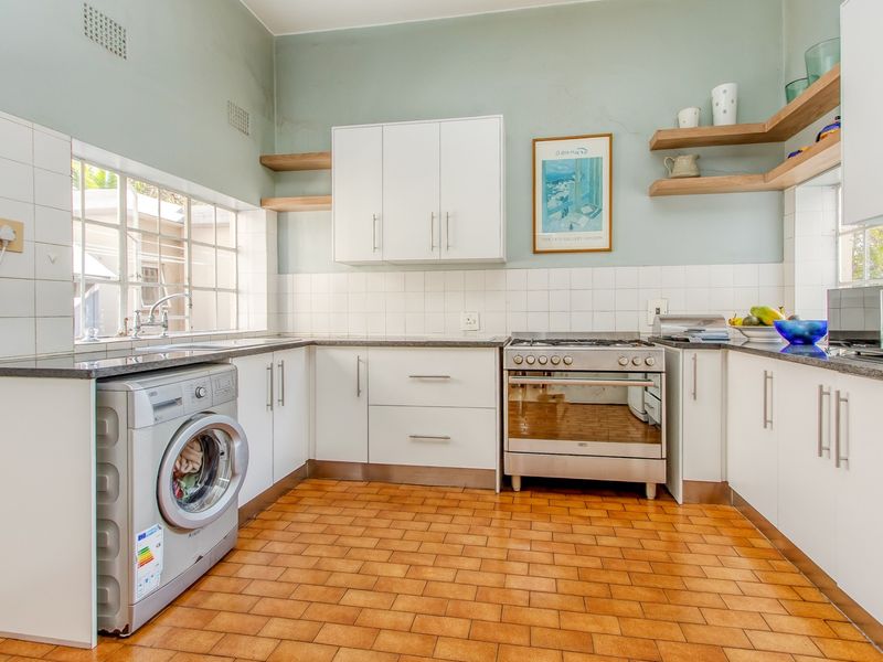 A functional kitchen featuring white cabinetry, granite countertops, a stainless steel stove, and classic terracotta floor tiles with ample natural light.