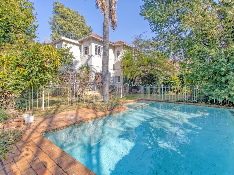 A view of the rear garden featuring a swimming pool with brick coping, enclosed by a metal fence, set against the two-story house exterior.