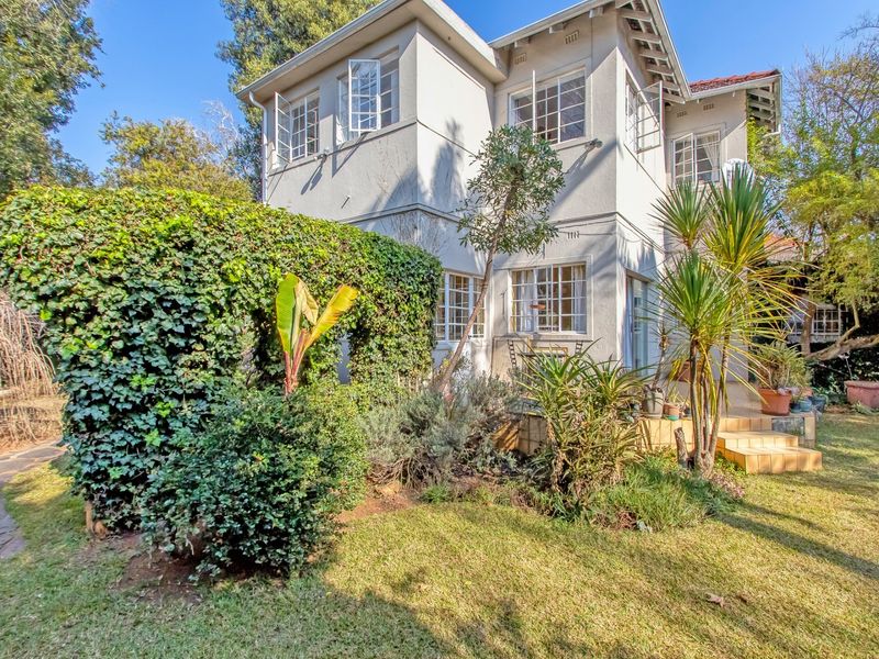Rear view of a two-story house featuring a tiled patio, established garden, and classic casement windows with a stucco exterior finish.