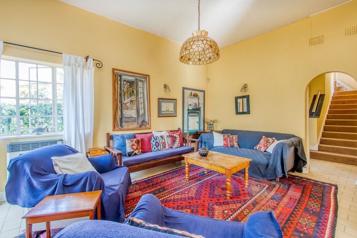 A spacious living room featuring yellow walls, a central pendant light, tiled flooring, and an arched entryway leading to a staircase.