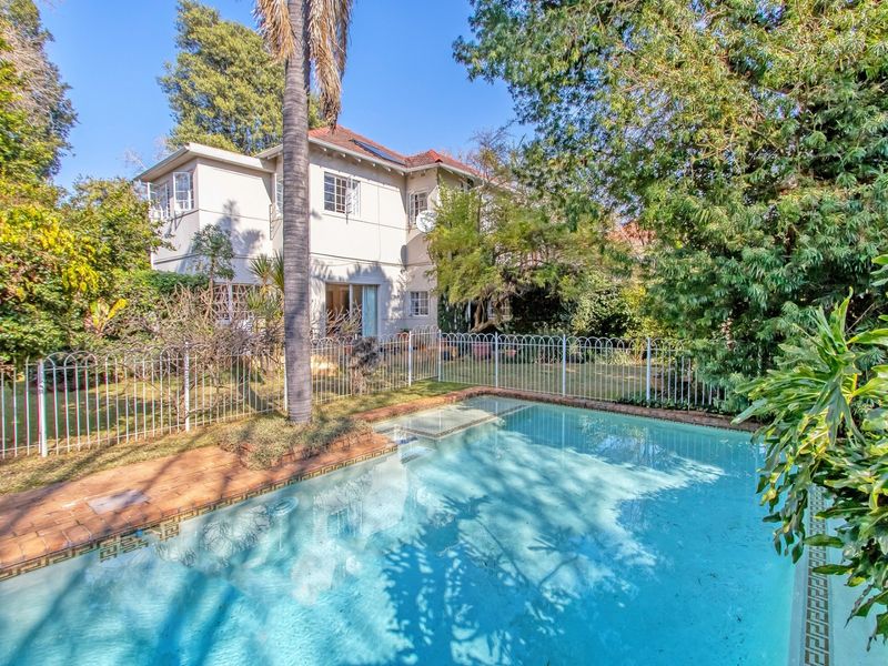A well-maintained backyard featuring a swimming pool with surrounding brick paving, metal safety fencing, and a view of the two-story residential dwelling.