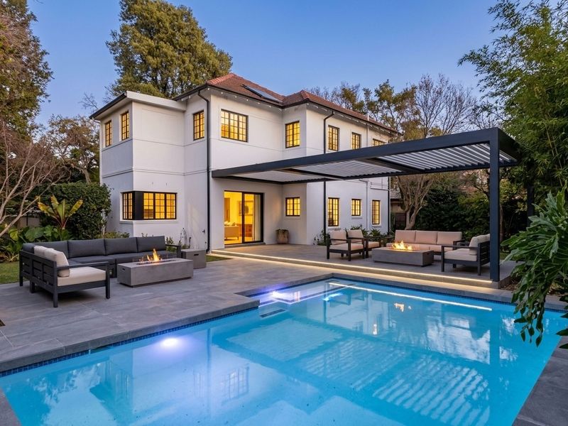 A beautifully landscaped rear exterior featuring a modern swimming pool, expansive tiled patio, and a louvered pergola, perfect for outdoor entertaining.