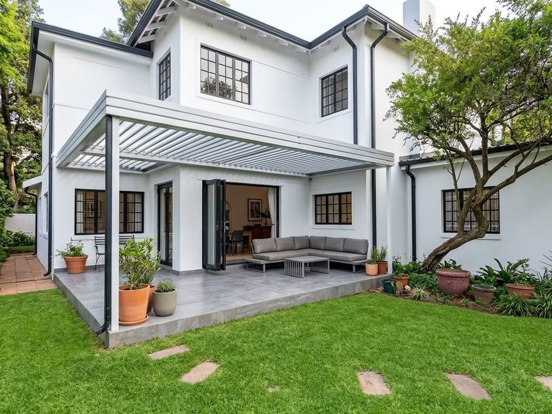 A well-maintained rear exterior featuring a modern louvered pergola over a tiled patio, bi-fold doors, and a landscaped garden.