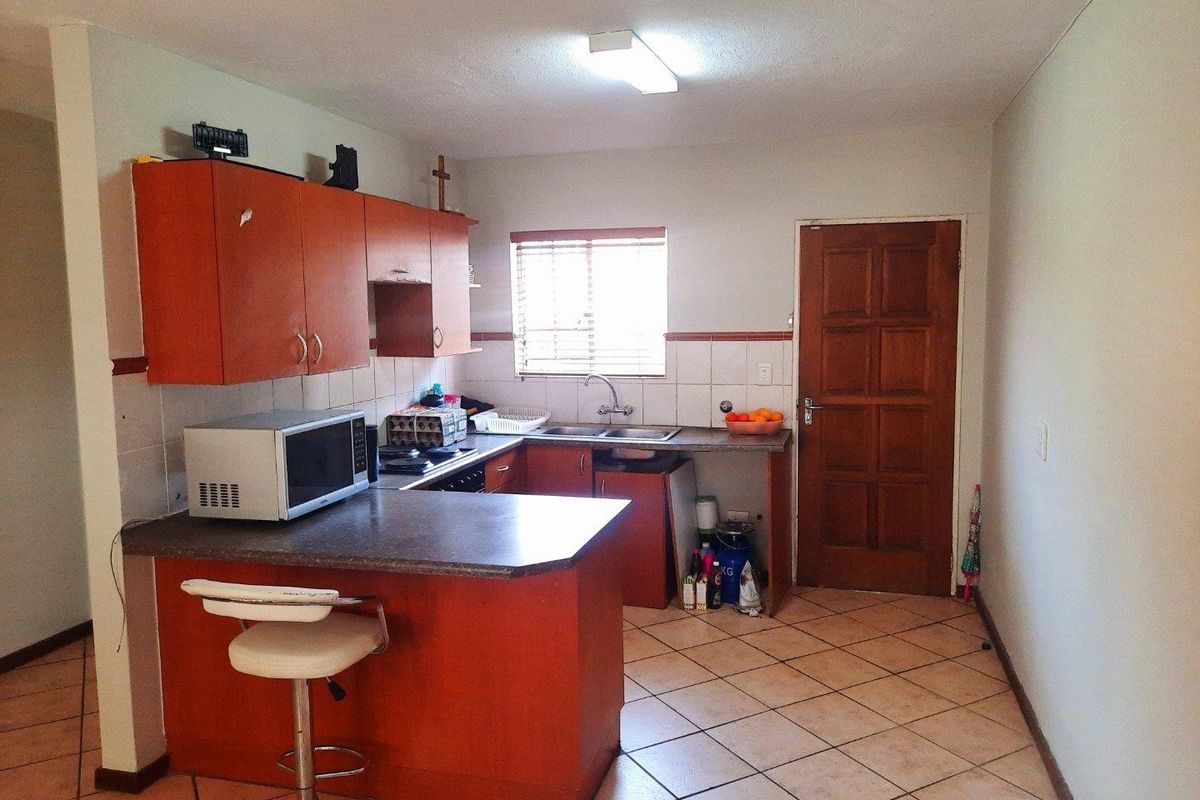 A functional kitchen featuring laminate cabinetry, tiled backsplash, and ceramic flooring, offering a practical layout with direct access to an exterior door.