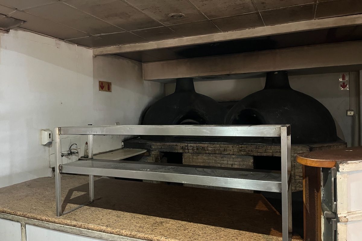 Commercial kitchen area featuring dual built-in wood-fired pizza ovens, stainless steel prep shelving, and stone countertops, requiring significant cleaning and refurbishment.