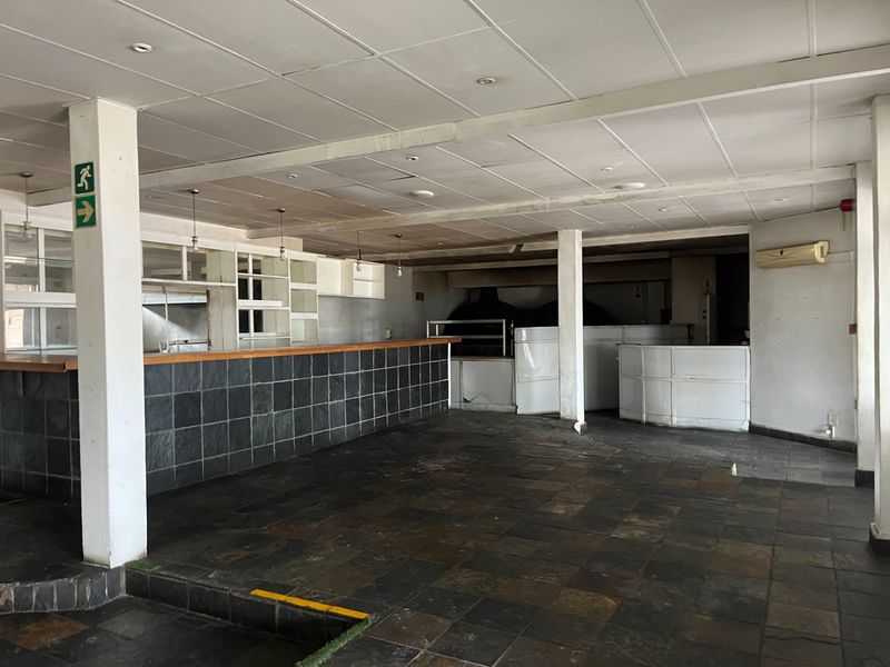An empty open-plan restaurant space featuring a large service counter, stone tile flooring, and a suspended ceiling, suitable for a commercial dining layout.