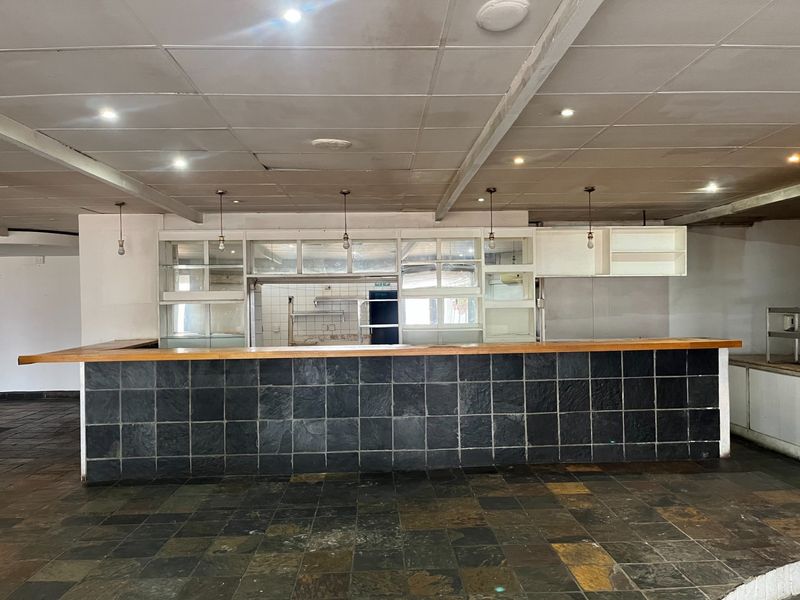 Spacious restaurant bar area featuring a slate-tiled counter, built-in shelving, and a suspended ceiling, offering a blank canvas for renovation.
