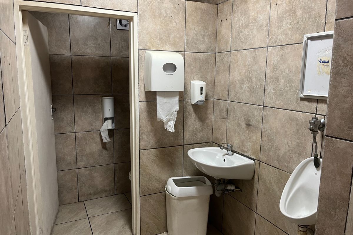 A functional commercial restroom featuring tiled walls and floors, equipped with a wall-mounted basin and a urinal.