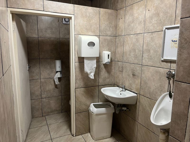 A functional commercial restroom featuring tiled walls and floors, equipped with a wall-mounted basin and a urinal.