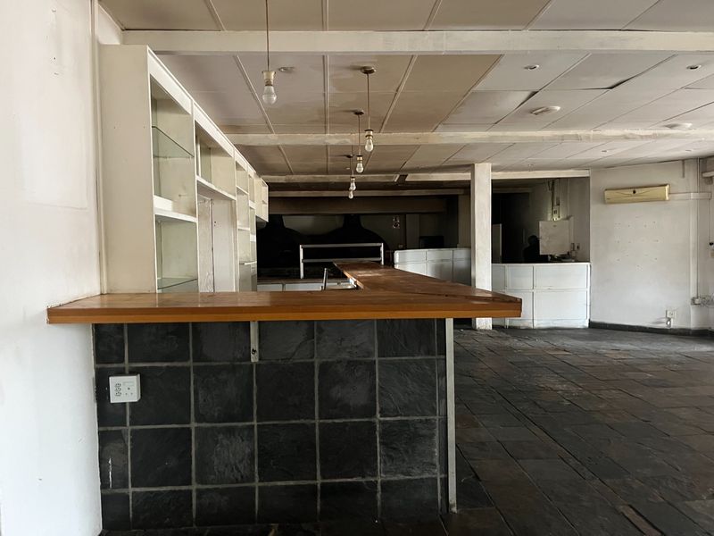 Vacant restaurant bar area featuring a built-in counter with slate tiling, stone flooring, and a suspended ceiling, ready for refurbishment.
