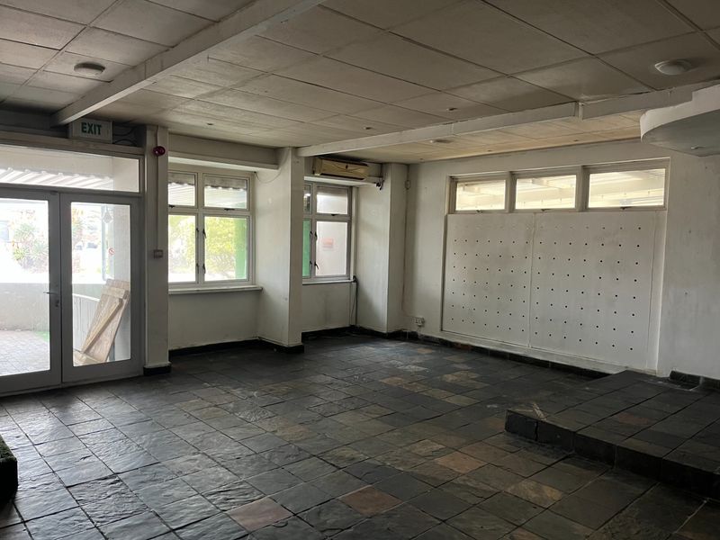 An empty open-plan restaurant space featuring dark tiled flooring, a suspended ceiling, split system air conditioning, and a raised platform area.