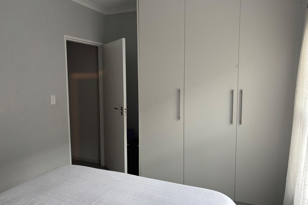 A bedroom featuring neutral walls, cove cornicing, and floor-to-ceiling built-in cupboards with modern handles.