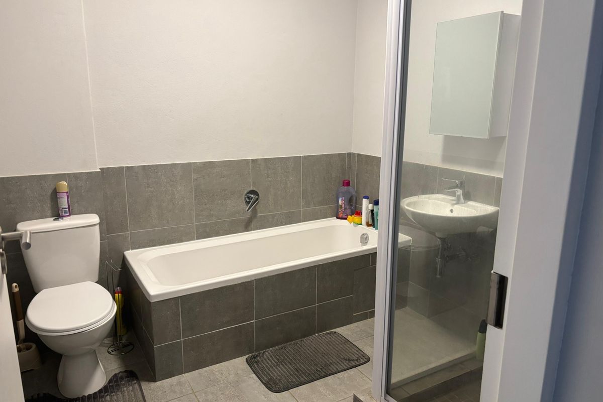 A functional bathroom featuring a bathtub, separate shower enclosure, pedestal sink, and neutral grey tiling throughout.