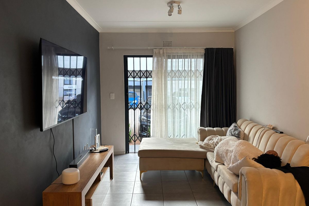 A well-maintained living room featuring tiled flooring, a security gate, and a sliding door providing access to the exterior.