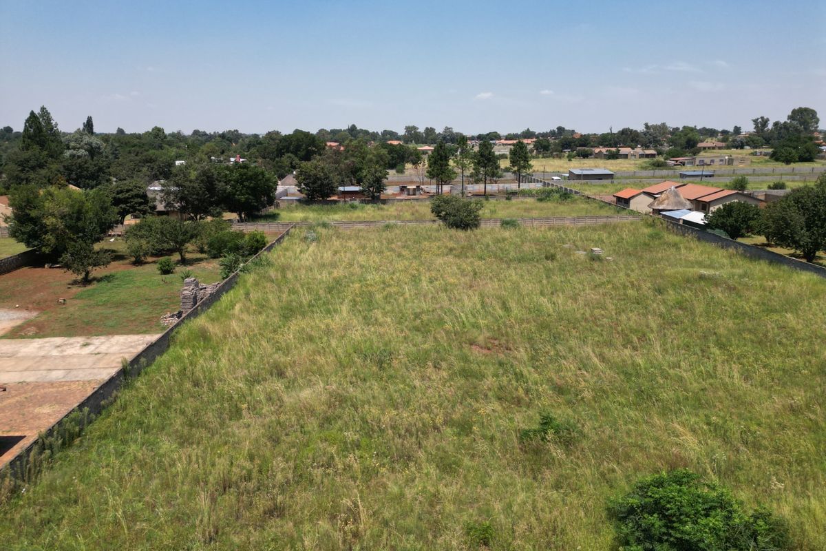 An aerial view of a large, vacant residential plot featuring perimeter walling and established surrounding neighborhood vegetation.