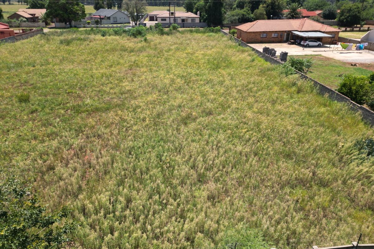 An elevated aerial view of a vacant residential plot, featuring perimeter walling and electric fencing, surrounded by established neighborhood properties.