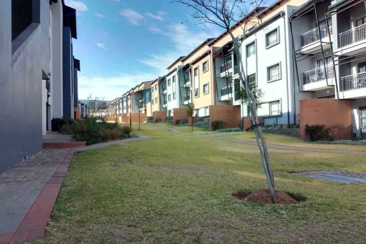 A view of the apartment complex exterior featuring landscaped communal lawns, paved pathways, and private balconies with brick detailing.