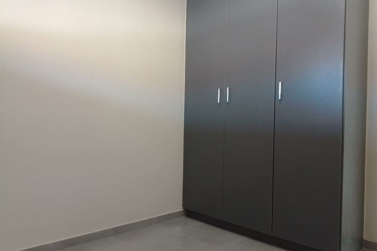 A clean, minimalist bedroom featuring modern dark grey built-in cupboards and neutral tiled flooring, offering a blank canvas for personalization.