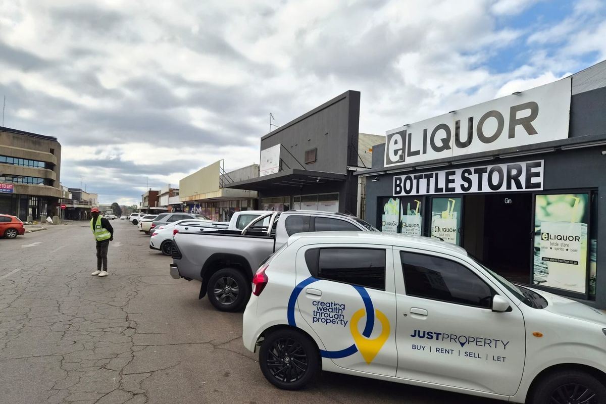 Street view of a commercial retail strip featuring a bottle store storefront with adjacent parking and paved road access.