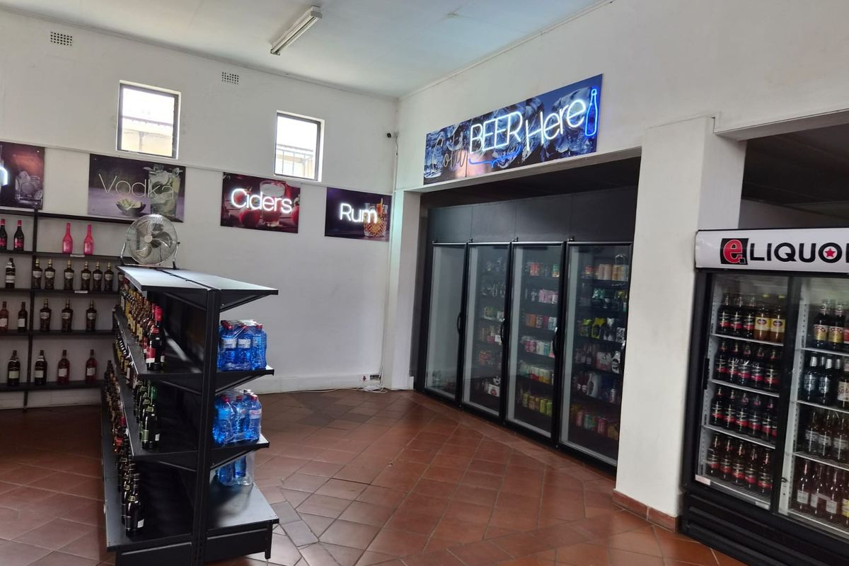 A retail liquor store interior featuring commercial refrigeration units, wall-mounted display shelving, and tiled flooring.